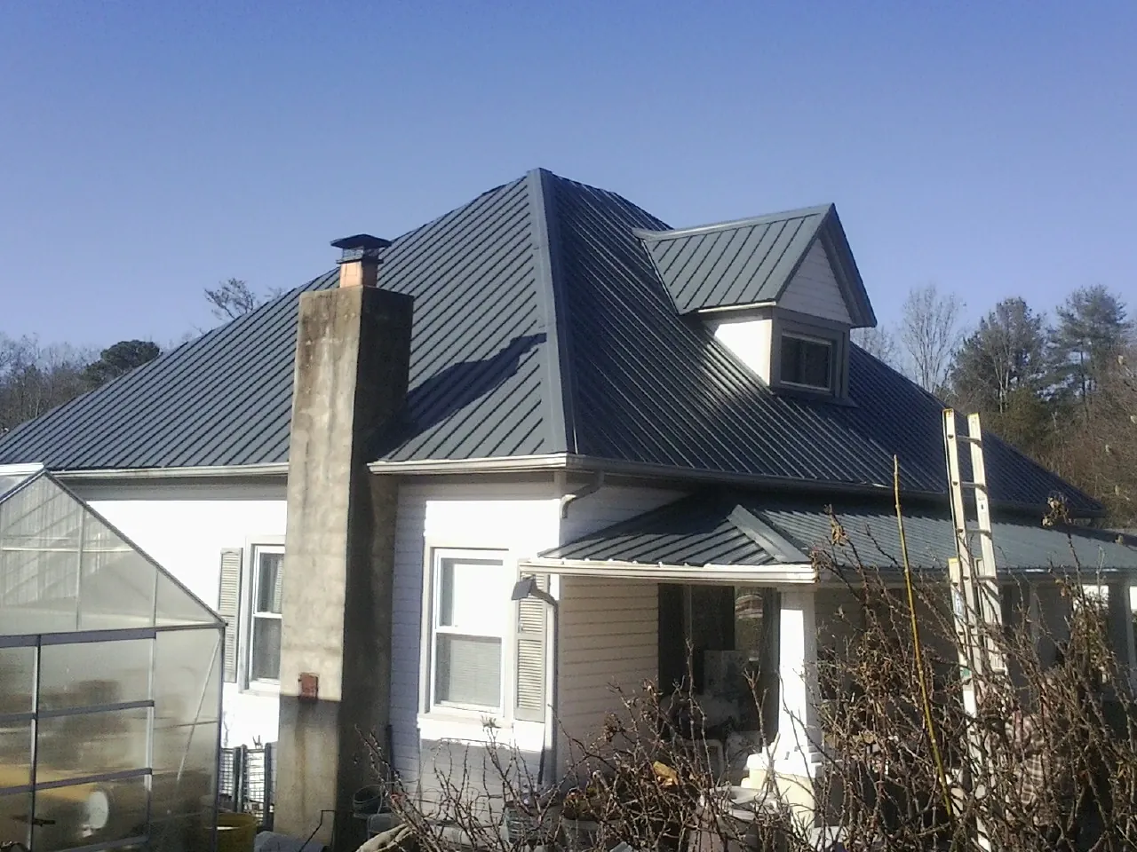 Dark blue standing seam metal roof on a white farmhouse with dormer — Slate & Tile Roof Repair by Roofing Brothers in Wesson