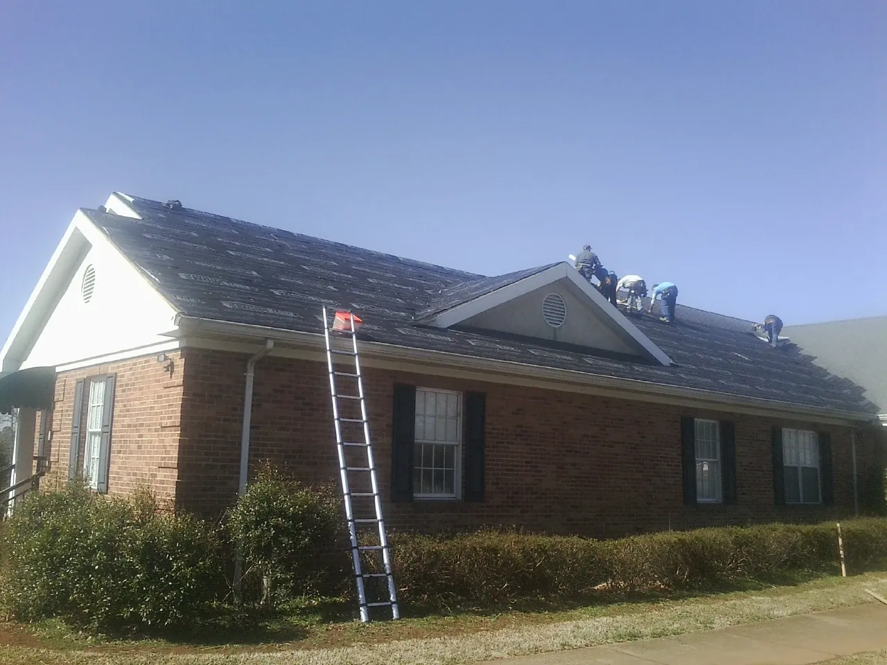 Crew tearing shingles off a brick ranch roof with a ladder set — Metal Roof Repair work by our crew in Wesson