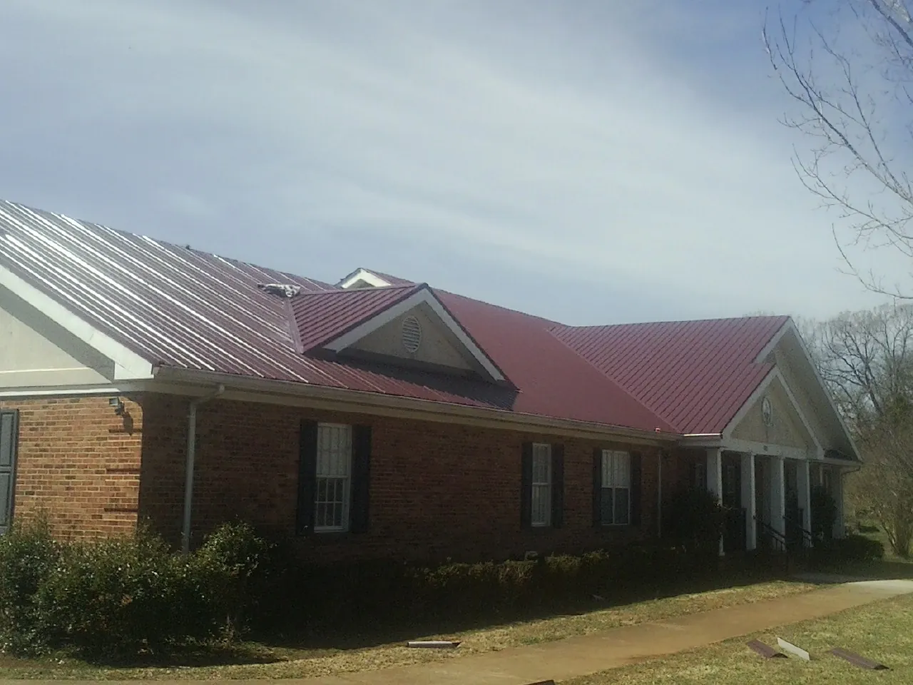 Red metal roof with gabled entries on a long brick building, from a Hail Damage Roof Repair job in Wesson