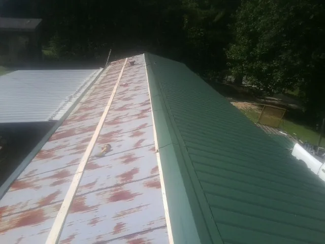 Old rusted panels beside newly installed green metal roofing — Wind Damage Roof Repair by Roofing Brothers in Wesson