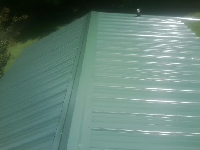 New green metal panels meeting at the ridge of a roof — Flat Roof Repair work by our crew in Wesson