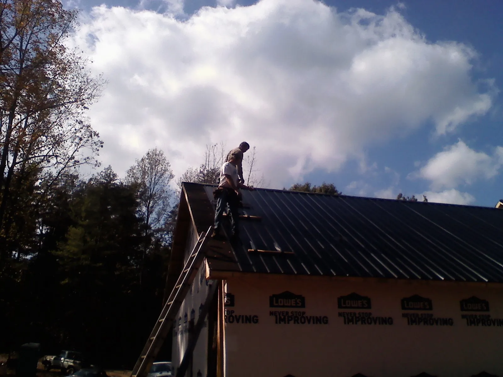 Roofer fastening dark metal panels high against a cloudy sky, from a Roof Inspection job in Wesson